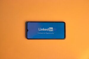 Smartphone mit dem LinkedIn-Logo auf dem Bildschirm vor orangefarbenem Hintergrund.