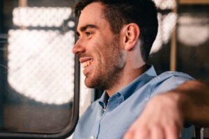 Mann im blauen Hemd in einer Straßenbahn; sein Gesicht ist scharf, die Hand im Vordergrund unscharf