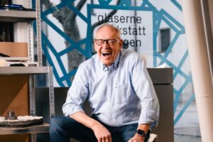 Lachender Interviewpartner mit kleinem Ansteckmikrofon am hellblauen Hemd in einer Werkstatt