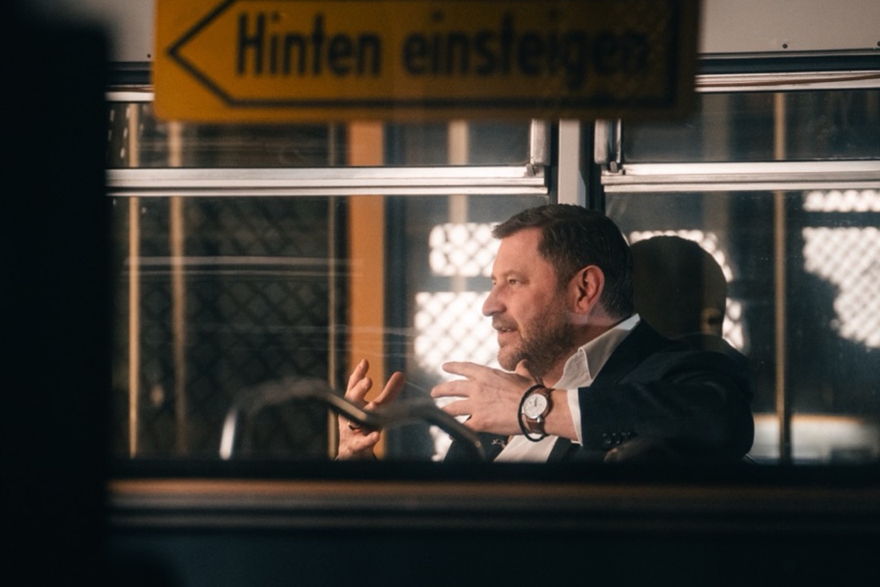 Mann spricht in einer historischen Straßenbahn; helle Fenster stehen einem dunklen Vordergrund gegenüber